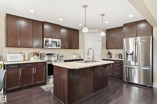 Kitchen featuring dark wood-finish cabinetry, stainless steel appliances, a center island with a sink, pendant lighting, and wood-finish flooring - 1564 36 Avenue Nw, Edmonton, AB 