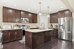 Kitchen featuring dark wood-finish cabinetry, stainless steel appliances, a center island with a sink, pendant lighting, and wood-finish flooring - 