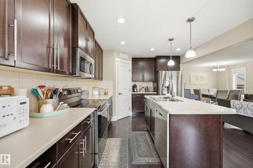 Dark wood-finish cabinetry, stainless steel appliances, light-toned countertops, pendant lighting, and wood-finish flooring - 1564 36 Avenue Nw, Edmonton, AB 