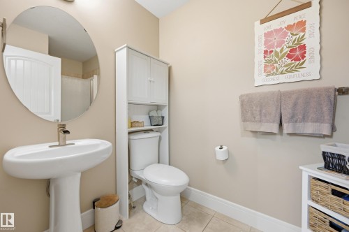 Pedestal sink with a brushed nickel faucet, oval mirror, and ceramic tile flooring - 1564 36 Avenue Nw, Edmonton, AB 