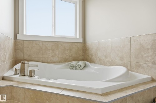 Built-in soaking tub with a stainless steel faucet, set within a tiled surround and illuminated by a large window - 1564 36 Avenue Nw, Edmonton, AB 