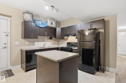 Kitchen featuring dark wood-finish cabinetry, light countertops, an island with integrated power, and tile flooring - 
