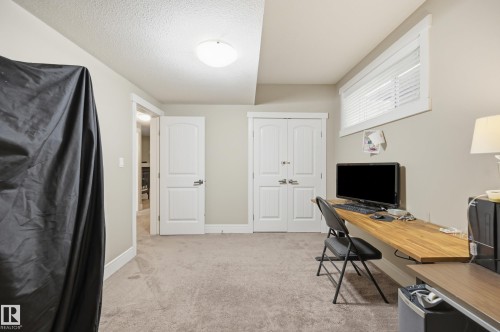 Carpeted flooring, a flush-mount ceiling light, white trim, a built-in wood-finish desk, and a horizontal window with blinds - 1564 36 Avenue Nw, Edmonton, AB 