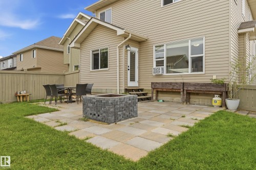 Rear exterior with beige horizontal siding, paver patio, integrated fire pit, and wood perimeter fencing - 1564 36 Avenue Nw, Edmonton, AB 