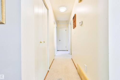Hallway featuring light-toned walls, built-in bi-fold closet doors with brass hardware, and a ceiling-mounted light fixture - 9 Hawkins Crescent, Sherwood Park, AB 