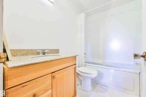 Light wood-finish vanity with a speckled countertop, a white drop-in sink, and a chrome faucet - 9 Hawkins Crescent, Sherwood Park, AB 