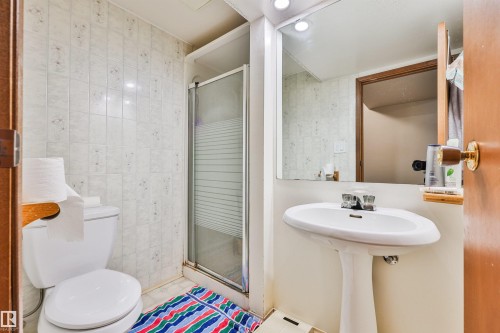 Pedestal sink with chrome faucet, wall-mounted mirror, ceramic tile walls, and a shower enclosure with sliding glass doors - 9 Hawkins Crescent, Sherwood Park, AB 