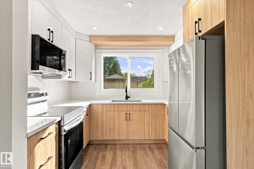 Galley kitchen with white upper cabinetry and wood-finish lower cabinetry, wood-finish flooring, and stainless steel appliances - 17325 85 Avenue Nw, Edmonton, AB 