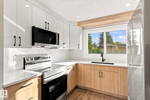 Contemporary kitchen featuring light wood-finish lower cabinetry, white upper cabinetry, stainless steel appliances, and a white countertop - 17325 85 Avenue Nw, Edmonton, AB 