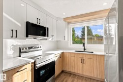 Contemporary kitchen featuring light wood-finish lower cabinetry, white upper cabinetry, stainless steel appliances, and a white countertop - 