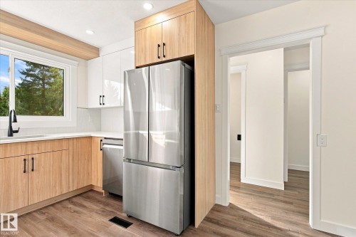 Modern kitchen featuring wood-finish lower cabinetry, white upper cabinetry, stainless steel appliances, and wood-finish flooring - 17325 85 Avenue Nw, Edmonton, AB 