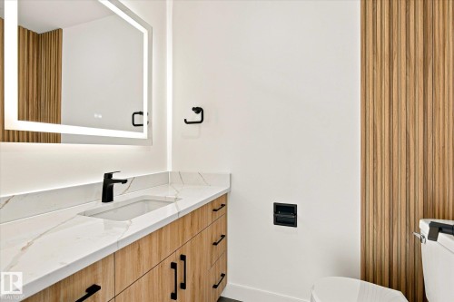 Vanity with a white countertop and integrated sink, matte black faucet, and wood-finish cabinetry - 17325 85 Avenue Nw, Edmonton, AB 