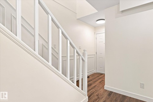 White painted staircase with wood-finish flooring, wainscoting, and a flush-mount ceiling light fixture - 17325 85 Avenue Nw, Edmonton, AB 