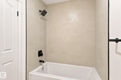 Bathtub with matte black fixtures, light-toned wall tiling, and a white paneled door - 17325 85 Avenue Nw, Edmonton, AB 