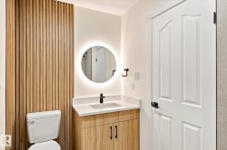 Bathroom featuring a wood slat accent wall, a floating vanity with a white countertop, a circular back-lit mirror, and a white paneled door with black hardware - 