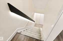 Modern staircase featuring a black angular handrail with integrated lighting, recessed wall lighting, carpeted treads, and wood-finish flooring - 