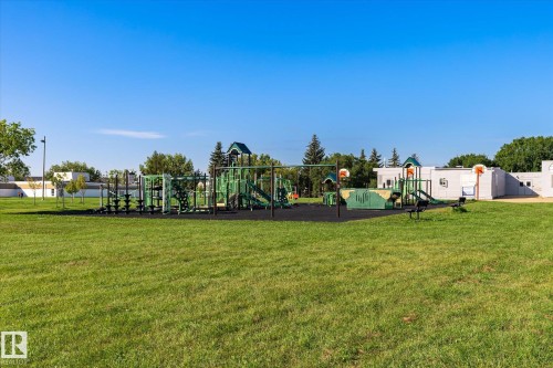 Expansive green space featuring a multi-component playground structure, integrated slides, swing sets, and basketball hoops, all set on a dark-toned safety surface - 17325 85 Avenue Nw, Edmonton, AB 