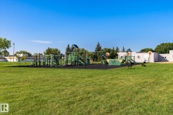 Expansive green space featuring a multi-component playground structure, integrated slides, swing sets, and basketball hoops, all set on a dark-toned safety surface - 