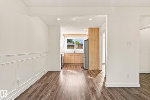 Wood-finish flooring throughout, white paneled wall detailing, recessed lighting, and kitchen with wood-tone cabinetry and stainless-steel appliances - 17325 85 Avenue Nw, Edmonton, AB 
