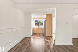 Wood-finish flooring throughout, white paneled wall detailing, recessed lighting, and kitchen with wood-tone cabinetry and stainless-steel appliances - 