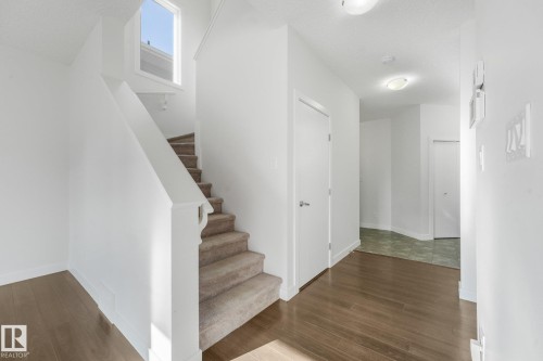 Carpeted staircase with a window and a landing, complemented by wood-finish flooring and flush mount lighting - 7832 Erasmus Wynd Nw, Edmonton, AB 