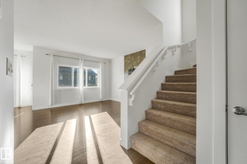 Hardwood-finish flooring, white painted walls, and an interior staircase with a carpeted runner and white railing - 7832 Erasmus Wynd Nw, Edmonton, AB 