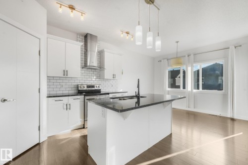 Kitchen featuring white cabinetry, stainless steel appliances, dark countertops, white subway tile backsplash, and wood-finish flooring - 7832 Erasmus Wynd Nw, Edmonton, AB 