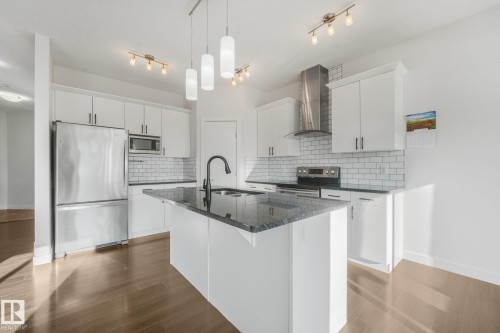 Kitchen featuring white cabinetry, stainless steel appliances, a center island with a dark countertop, subway tile backsplash, and wood-finish flooring - 7832 Erasmus Wynd Nw, Edmonton, AB 