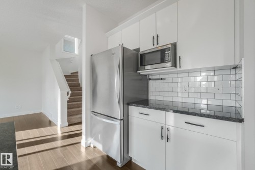 White cabinetry with dark hardware, stainless steel appliances, subway tile backsplash, dark countertop, and wood-finish flooring - 7832 Erasmus Wynd Nw, Edmonton, AB 