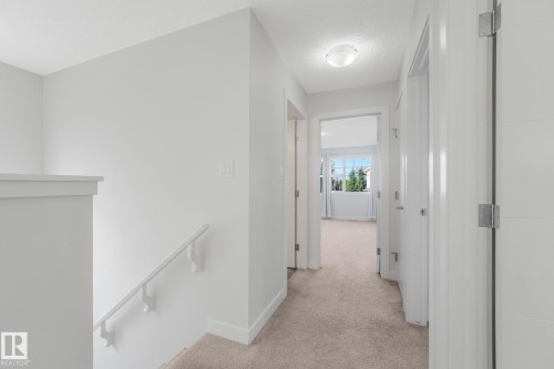 Hallway featuring light neutral-toned carpet, white walls, and flush-mount ceiling lighting - 7832 Erasmus Wynd Nw, Edmonton, AB 