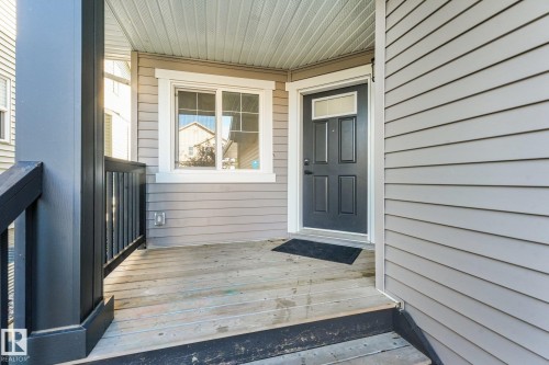 Front entry featuring horizontal siding, a paneled door with transom window, and a wood-finish porch with dark railings - 7832 Erasmus Wynd Nw, Edmonton, AB 