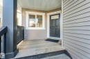 Front entry featuring horizontal siding, a paneled door with transom window, and a wood-finish porch with dark railings - 7832 Erasmus Wynd Nw, Edmonton, AB 