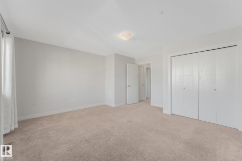Spacious room featuring neutral carpeting, light-toned walls, and a ceiling-mounted light fixture - 7832 Erasmus Wynd Nw, Edmonton, AB 