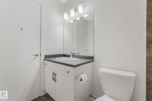 White vanity with a dark countertop, white integrated sink, and an overhead three-bulb light fixture - 7832 Erasmus Wynd Nw, Edmonton, AB 