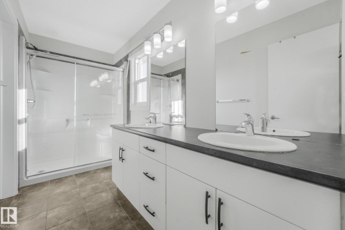 Dual vanity with integrated sinks, dark countertop, and white cabinetry with matte black hardware - 7832 Erasmus Wynd Nw, Edmonton, AB 