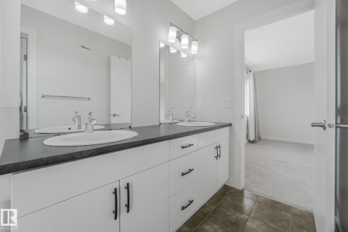 Dual-sink vanity with a dark countertop and white cabinetry - 7832 Erasmus Wynd Nw, Edmonton, AB 