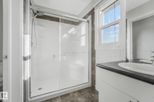 Glass-enclosed shower with a handheld shower head, a single vanity with an integrated sink, and an operable window - 7832 Erasmus Wynd Nw, Edmonton, AB 