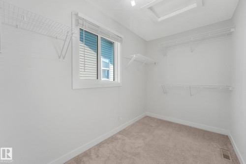 Walk-in closet featuring wire shelving, a window with blinds, and light-colored carpeting - 7832 Erasmus Wynd Nw, Edmonton, AB 