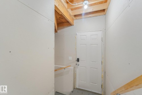 Exposed wood ceiling beams, unfinished drywall, white paneled door, black digital door lock - 7832 Erasmus Wynd Nw, Edmonton, AB 