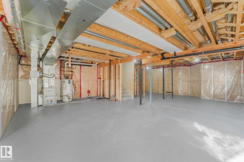 Unfinished lower level with exposed wood joists and structural beams, painted concrete flooring, and an installed furnace - 7832 Erasmus Wynd Nw, Edmonton, AB 