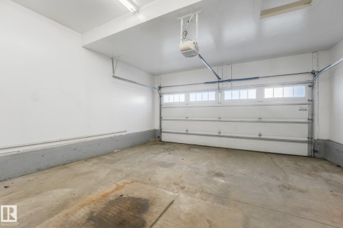 Attached garage with concrete flooring, white overhead sectional door featuring transom windows, and an automatic garage door opener - 7832 Erasmus Wynd Nw, Edmonton, AB 
