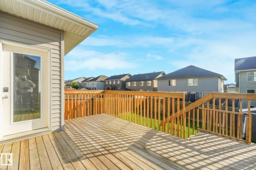 Expansive wood-finish deck with railing and stairs, featuring a screen door entry and siding exterior - 7832 Erasmus Wynd Nw, Edmonton, AB 