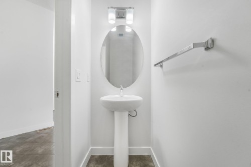 Pedestal sink with chrome faucet, oval mirror, chrome light fixture, and chrome towel bar - 7832 Erasmus Wynd Nw, Edmonton, AB 