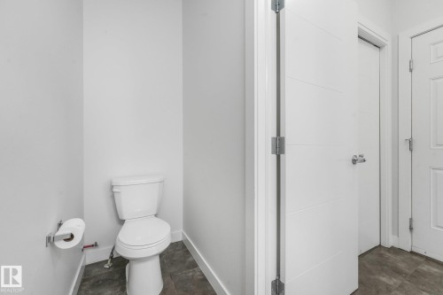 White toilet, dark gray floor tile, white walls, modern panel door - 7832 Erasmus Wynd Nw, Edmonton, AB 