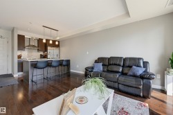 Open-concept living space featuring wood-finish flooring, a kitchen island with seating, pendant lighting, stainless steel appliances, and dark wood cabinetry - 