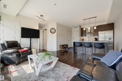 Open-concept living area featuring rich wood-finish flooring, a contemporary kitchen with stainless steel appliances, a breakfast bar with pendant lighting, and multiple recessed light fixtures - 