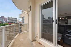 Outdoor balcony featuring a glass panel railing, concrete flooring, and an exterior wall light fixture - 