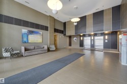 Spacious lobby featuring high ceilings, light-toned floor tiling, two pendant light fixtures, and a textured accent wall with dark grey paneling - 