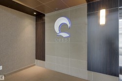 Entryway featuring a prominent illuminated brand logo, large format floor tiling, a wall-mounted light fixture, and textured wall coverings - 
