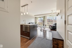 Open-concept living space featuring wood-finish flooring, a kitchen island with integrated stainless steel dishwasher, pendant lighting, and floor-to-ceiling windows - 